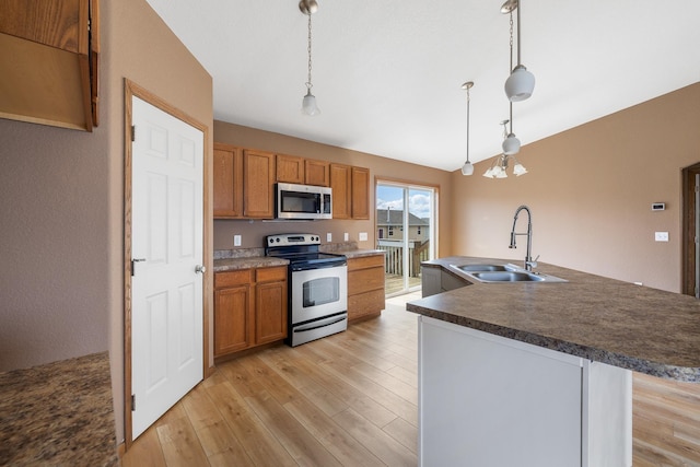 kitchen with stainless steel appliances, a sink, dark countertops, brown cabinets, and hanging light fixtures