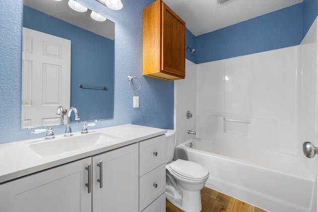 full bathroom with toilet, shower / bathtub combination, wood finished floors, a textured wall, and vanity