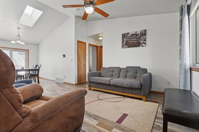 living area featuring a skylight, baseboards, visible vents, and ceiling fan with notable chandelier