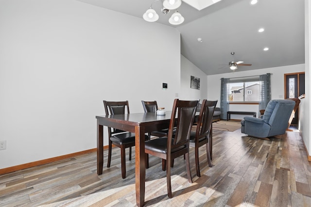 dining room featuring lofted ceiling with skylight, baseboards, wood finished floors, and ceiling fan with notable chandelier