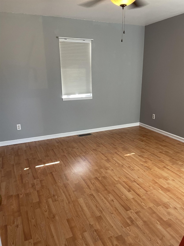 unfurnished room with baseboards, a ceiling fan, wood finished floors, and visible vents