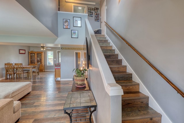 stairs with ceiling fan, a high ceiling, wood finished floors, and baseboards