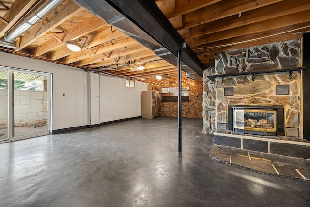 basement featuring baseboards, a stone fireplace, and stainless steel refrigerator with ice dispenser