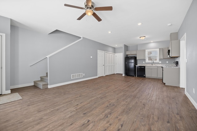 unfurnished living room featuring dark wood-style floors, a sink, visible vents, a ceiling fan, and stairs