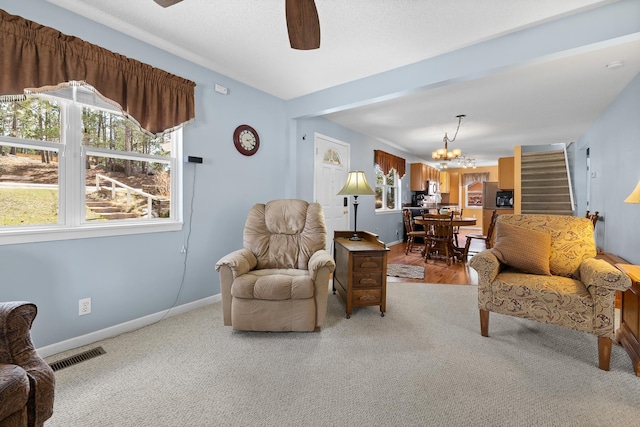 living room featuring baseboards, visible vents, light colored carpet, ceiling fan with notable chandelier, and stairway