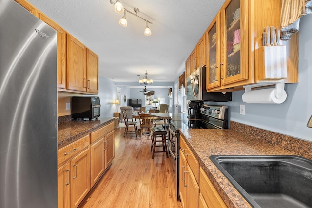 kitchen featuring a sink, brown cabinetry, glass insert cabinets, light wood-style flooring, and appliances with stainless steel finishes