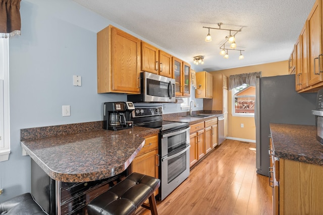 kitchen with stainless steel appliances, a sink, glass insert cabinets, light wood-style flooring, and a textured ceiling