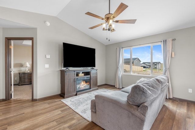 living area with a glass covered fireplace, vaulted ceiling, light wood-type flooring, and ceiling fan