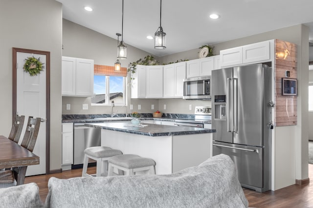 kitchen with white cabinets, dark countertops, vaulted ceiling, a kitchen island, and appliances with stainless steel finishes