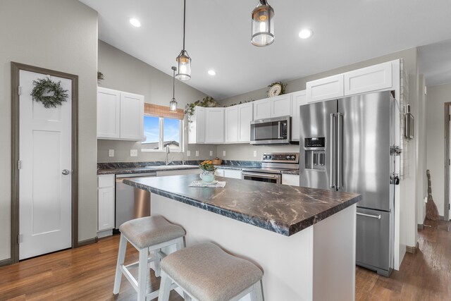 kitchen with a center island, dark countertops, a sink, stainless steel appliances, and white cabinetry