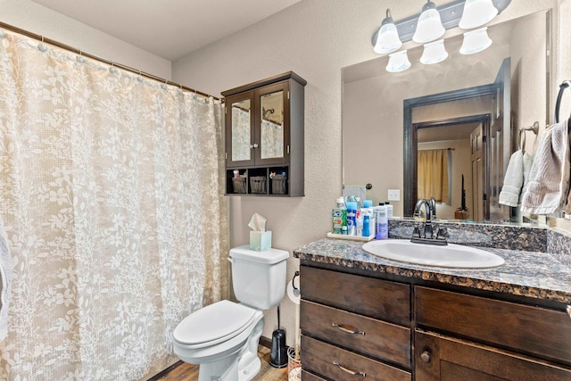 full bath with toilet, vanity, a textured wall, and wood finished floors