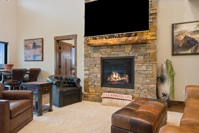 living area with a high ceiling, a stone fireplace, and carpet