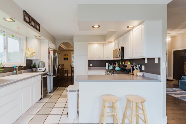 kitchen with white cabinets, stainless steel appliances, a peninsula, and arched walkways