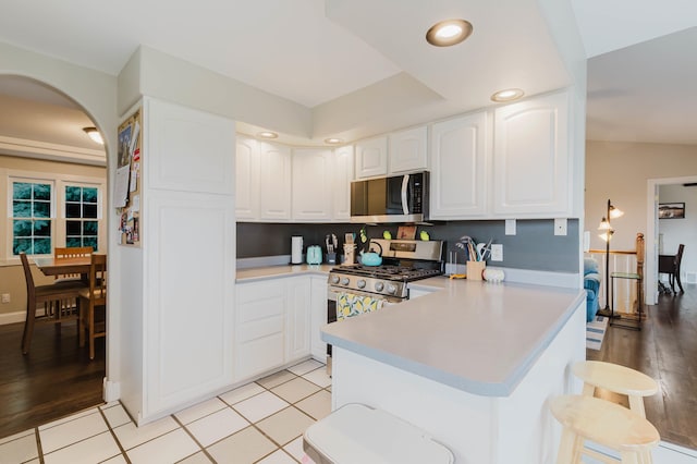 kitchen with white cabinetry, a breakfast bar, stainless steel appliances, light countertops, and a peninsula