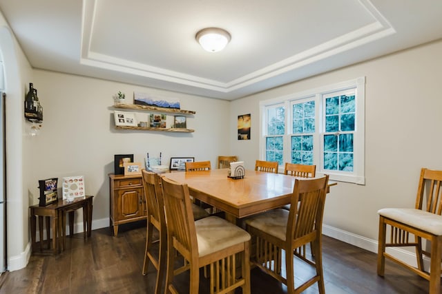 dining area featuring dark wood-type flooring, a raised ceiling, and baseboards