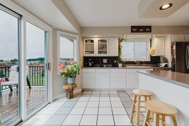 kitchen featuring glass insert cabinets, freestanding refrigerator, light tile patterned floors, white cabinets, and a sink