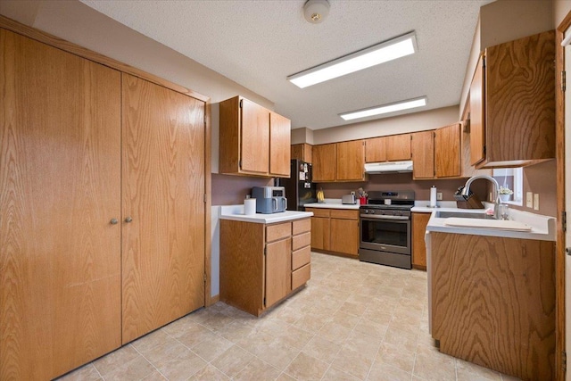 kitchen with brown cabinetry, light countertops, a sink, stainless steel range oven, and under cabinet range hood