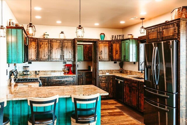 kitchen with a peninsula, light stone countertops, stainless steel fridge, dishwasher, and hanging light fixtures
