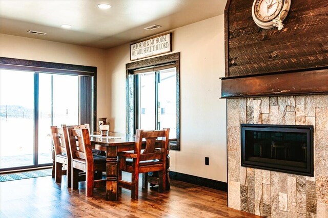 dining area featuring visible vents, baseboards, a glass covered fireplace, and wood finished floors