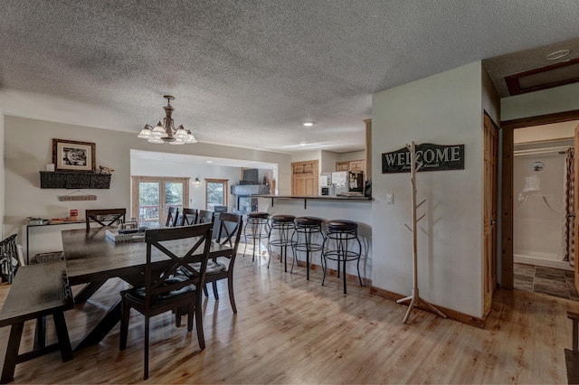 dining area with a textured ceiling, baseboards, a notable chandelier, and light wood-style floors
