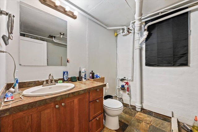 bathroom featuring walk in shower, toilet, vanity, and stone finish floor