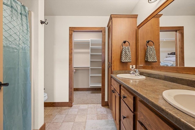 full bath with a sink, a walk in closet, toilet, and baseboards
