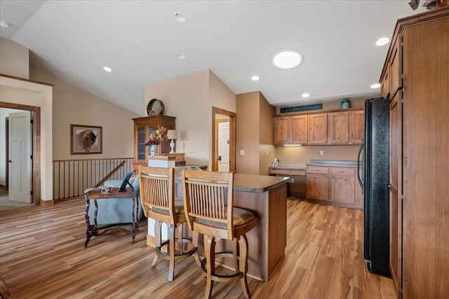 kitchen with vaulted ceiling, light wood finished floors, a breakfast bar, and freestanding refrigerator