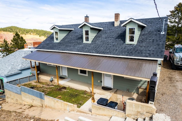 view of front facade with a shingled roof, a patio, a chimney, and fence