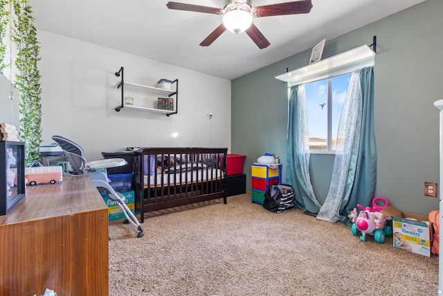bedroom featuring a nursery area, ceiling fan, and carpet floors