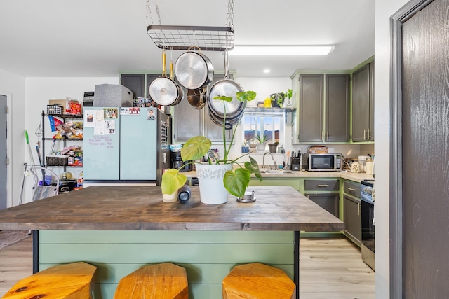 kitchen with light wood-style flooring, green cabinets, wooden counters, a sink, and appliances with stainless steel finishes