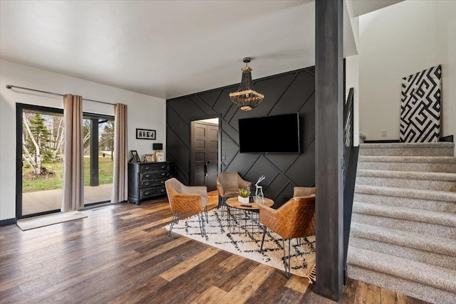 living area featuring an accent wall, wood finished floors, stairway, and a chandelier