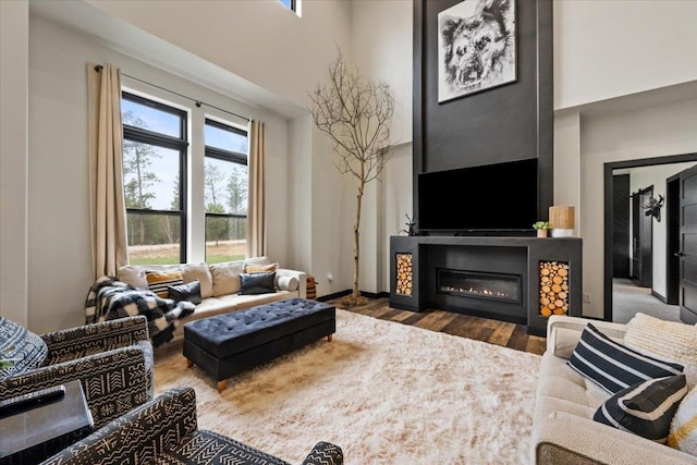 living room featuring wood finished floors, a glass covered fireplace, a high ceiling, and baseboards