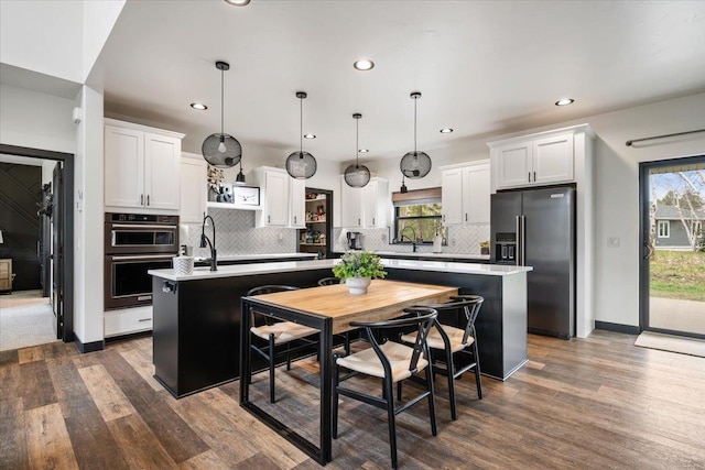 kitchen with high end refrigerator, a center island with sink, dark wood finished floors, double wall oven, and white cabinetry