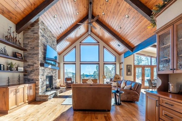 living area with beam ceiling, a stone fireplace, hardwood / wood-style floors, wooden ceiling, and high vaulted ceiling