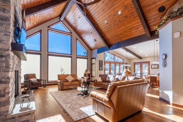living room featuring beam ceiling, wood-type flooring, a stone fireplace, wood ceiling, and high vaulted ceiling
