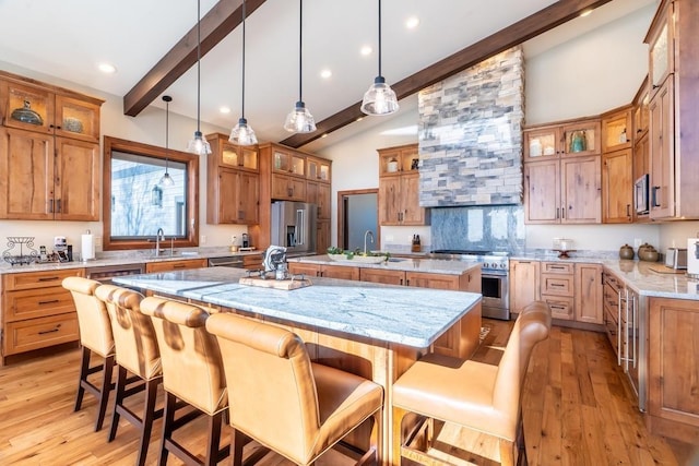 kitchen with high quality appliances, a large island with sink, brown cabinets, light wood-style flooring, and recessed lighting