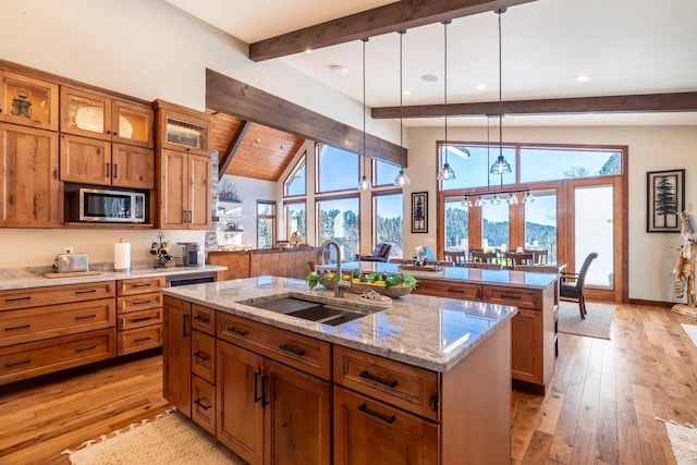 kitchen featuring a sink, brown cabinets, stainless steel microwave, a kitchen island with sink, and recessed lighting