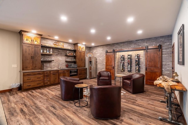 wine room with bar with sink, a barn door, dark wood-type flooring, recessed lighting, and baseboards