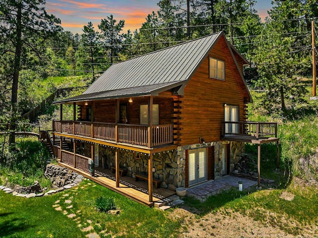 rear view of property featuring french doors, log siding, stone siding, a standing seam roof, and a wooden deck