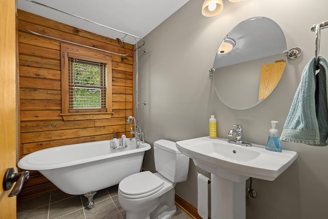 full bathroom with rustic walls, toilet, a freestanding bath, tile patterned floors, and a sink