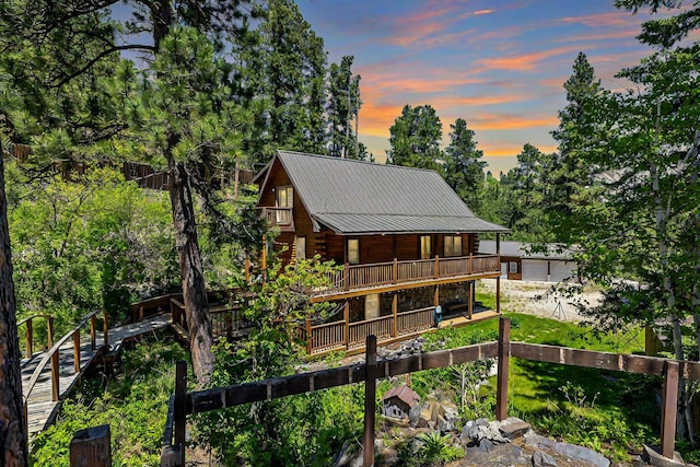 back of property at dusk with fence, metal roof, a wooden deck, log siding, and view of scattered trees
