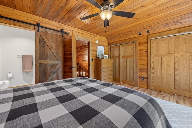 unfurnished bedroom featuring wooden walls, a barn door, light wood-style flooring, two closets, and a ceiling fan