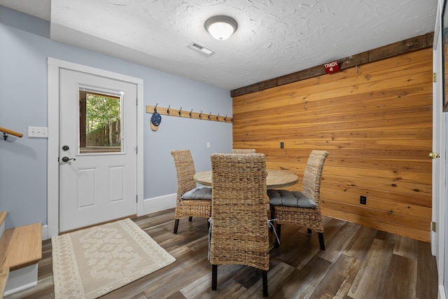 dining area with wood finished floors, wooden walls, and a textured ceiling