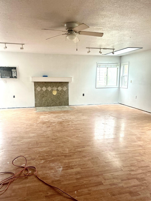 unfurnished living room featuring track lighting, a ceiling fan, wood finished floors, and a textured ceiling