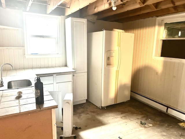 1222 9th Ave, Belle Fourche, SD 57717 - kitchen with white fridge with ice dispenser, a sink, tile countertops, wood walls, and white cabinets