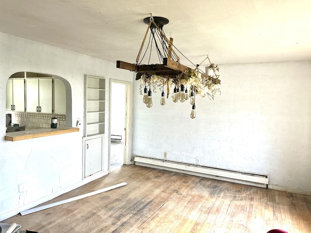 unfurnished dining area featuring a baseboard radiator, arched walkways, and wood finished floors