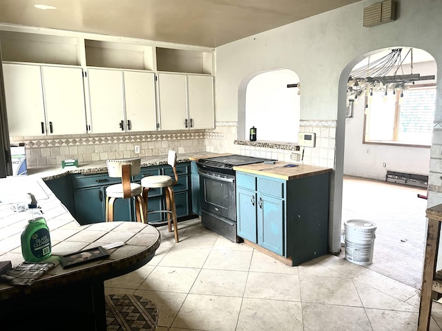 kitchen featuring black electric range, arched walkways, backsplash, light countertops, and light tile patterned floors