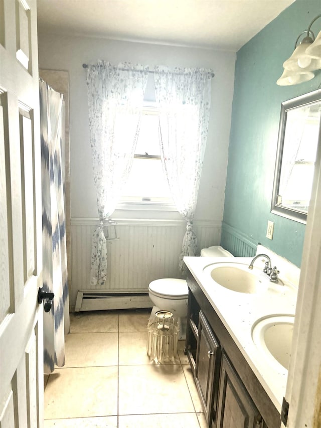 bathroom with baseboard heating, tile patterned floors, toilet, double vanity, and wainscoting