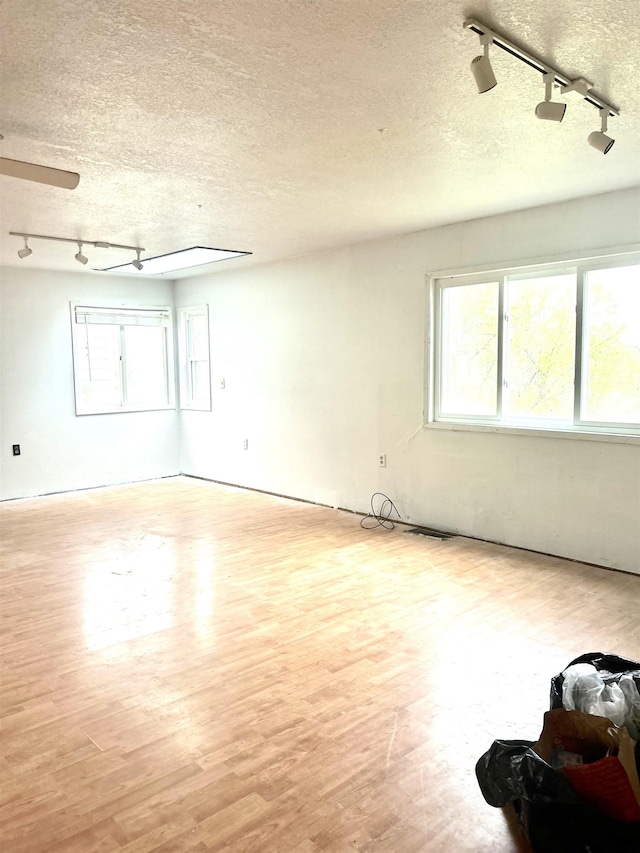spare room featuring rail lighting, wood finished floors, and a textured ceiling