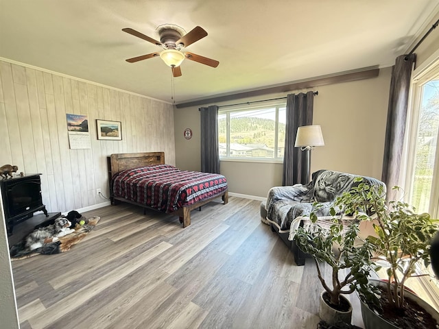 bedroom featuring baseboards, multiple windows, wood finished floors, wood walls, and ornamental molding